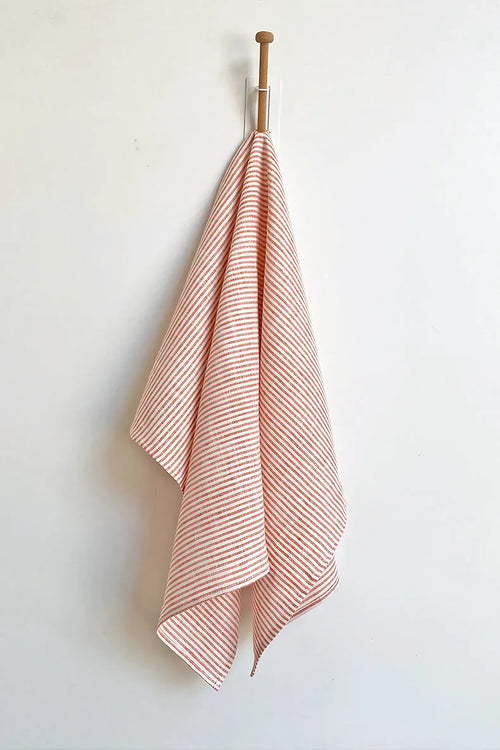 Pink and white striped towel hanging on a wooden hook against a white wall.