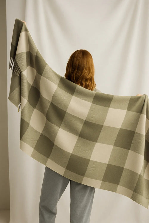 Person holding a green and white checkered blanket against a plain background