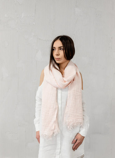 Cabana Linen Scarf in soft blush, loosely wrapped around a woman, showcasing its lightweight and breathable fabric.