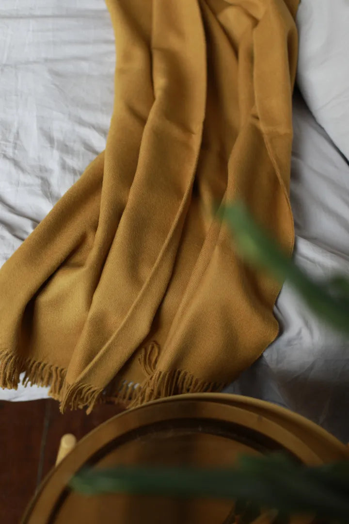 Paris Baby Alpaca Throw in mustard yellow draped over a bed