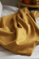 Paris Baby Alpaca Throw in mustard yellow casually folded on a white bed.