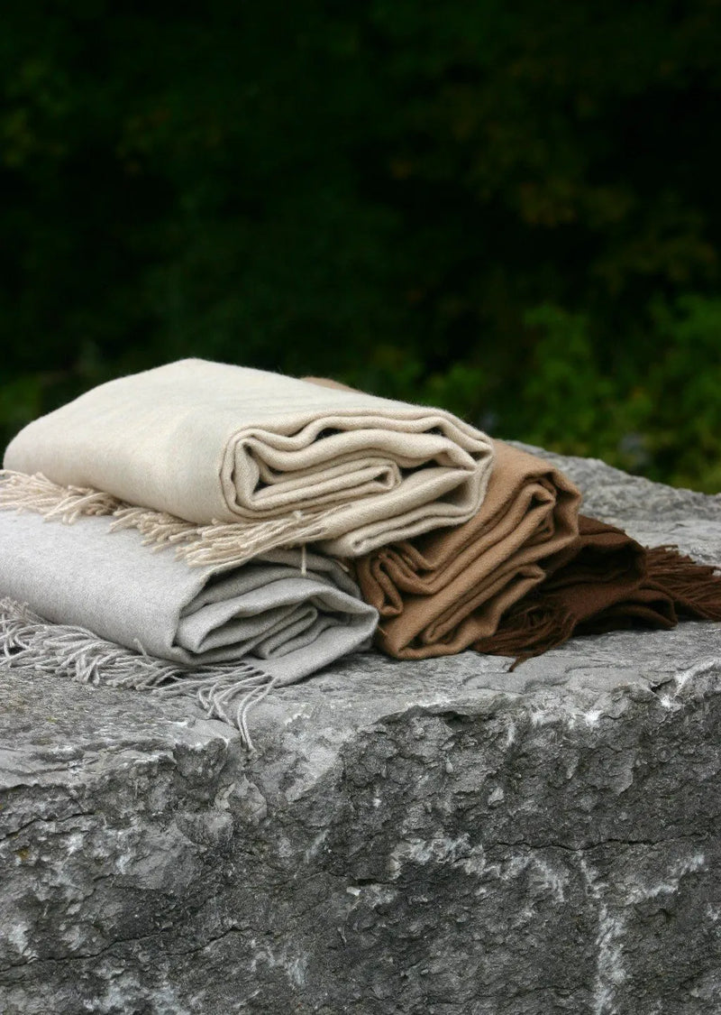 Three Paris Baby Alpaca Throws in neutral tones, stacked on a textured rock