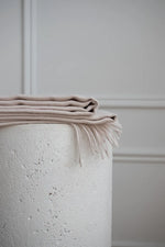 Stack of Paris Baby Alpaca Throws on a textured stone pedestal, emphasizing lightweight elegance.