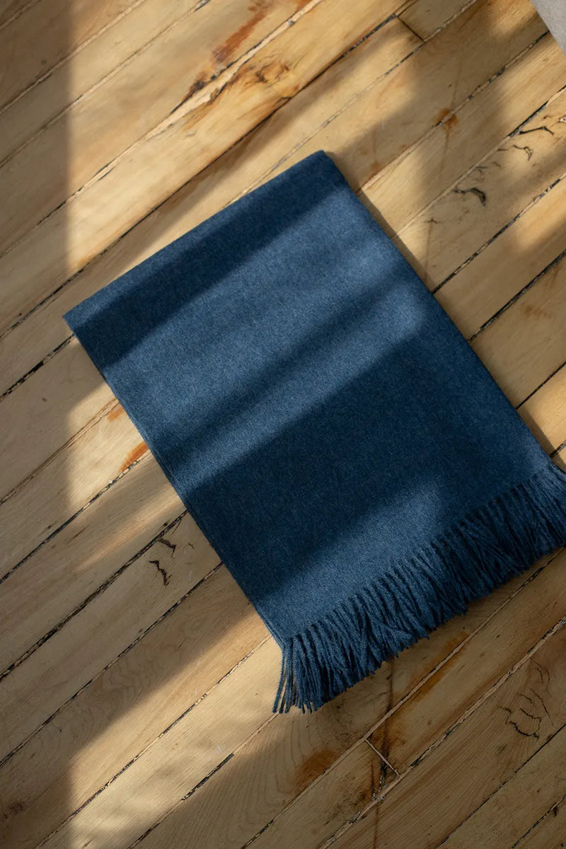 Paris Baby Alpaca Throw in deep blue shade, placed on a wooden floor with natural sunlight.