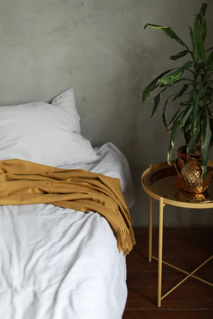 Paris Baby Alpaca Throw in mustard color, elegantly placed on a bed beside a gold table