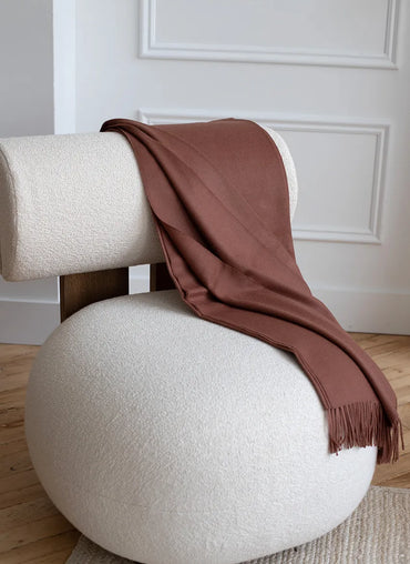 Paris Baby Alpaca Throw in warm brown elegantly placed on a modern white chair