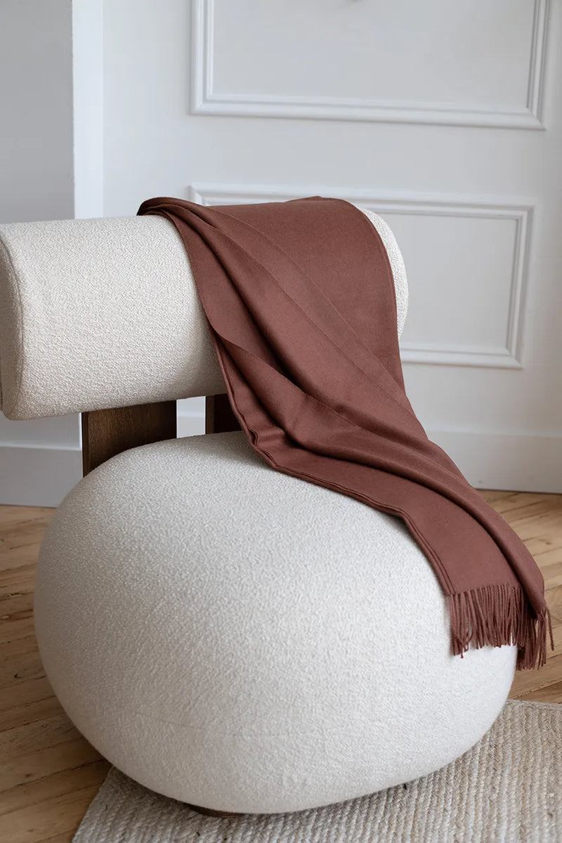 Paris Baby Alpaca Throw in warm brown elegantly placed on a modern white chair