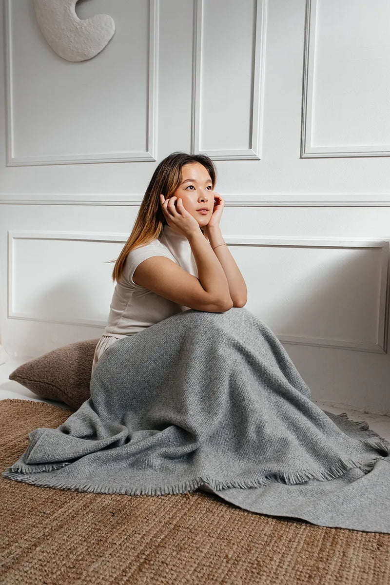 Woman sitting on the floor, wrapped in a soft gray Upland Textured Baby Alpaca Throw